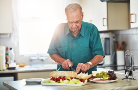 A aged man cutting fruits in kitchen